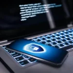 Smartphone with security shield on a laptop displaying code, representing mobile cybersecurity solutions.