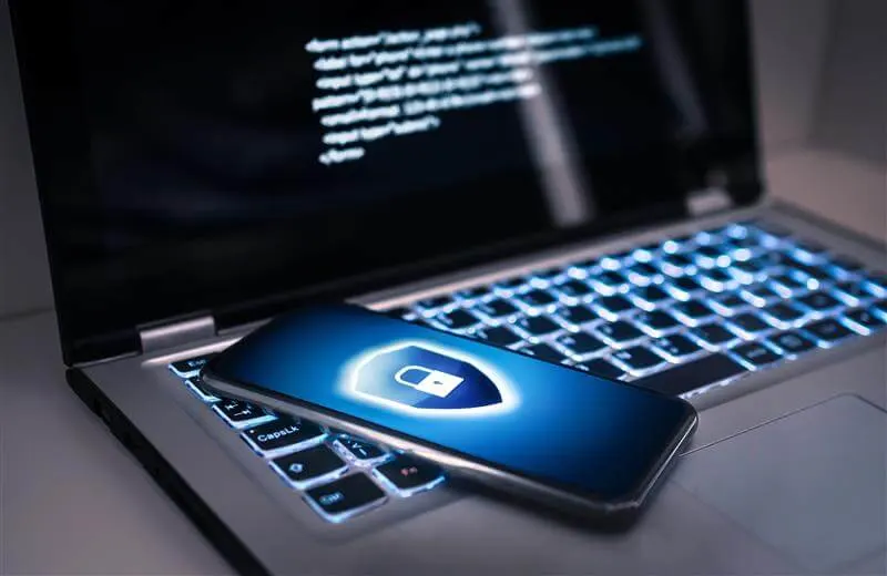 Smartphone with security shield on a laptop displaying code, representing mobile cybersecurity solutions.