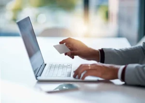 Person holding a card while using a laptop, representing secure online transactions with our cybersecurity solutions.